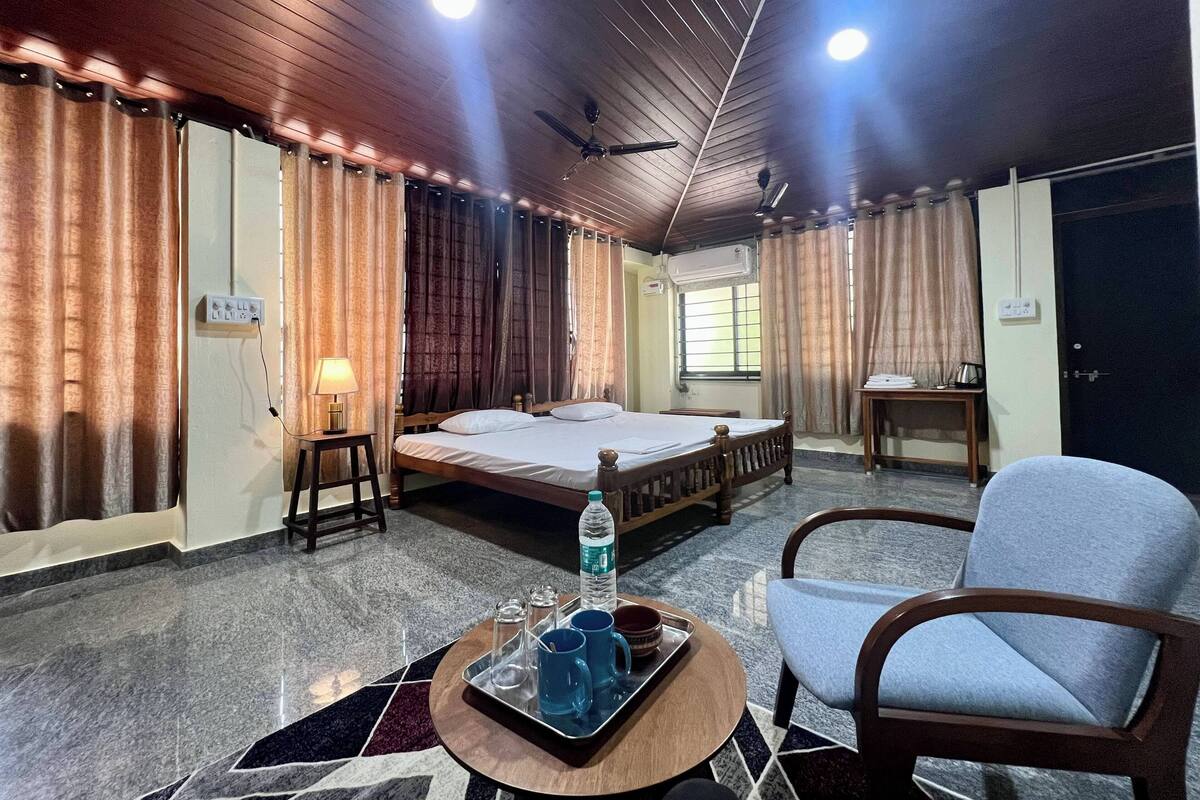 A hotel room with a bed, a chair, a table with a tray of items, and curtains.