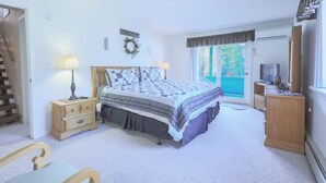 Un dormitorio con cama, cómoda, mesita de noche, lámpara, silla y vistas al exterior.