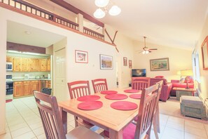 A dining area with a wooden table and chairs, a kitchen in the background, and a staircase leading to an upper level. - Official Seasons RMC Condo 02F - 1 bedroom + loft - sleeps 8 - No Fees (Bartlett)