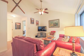 A living room with a red leather sofa, a wooden coffee table, a television, and a ceiling fan. - Official Seasons RMC Condo 02F - 1 bedroom + loft - sleeps 8 - No Fees (Bartlett)
