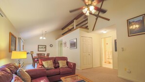 A living room with a red leather sofa, a wooden coffee table, a dining area with a table and chairs, a staircase, and a door leading to a bathroom.