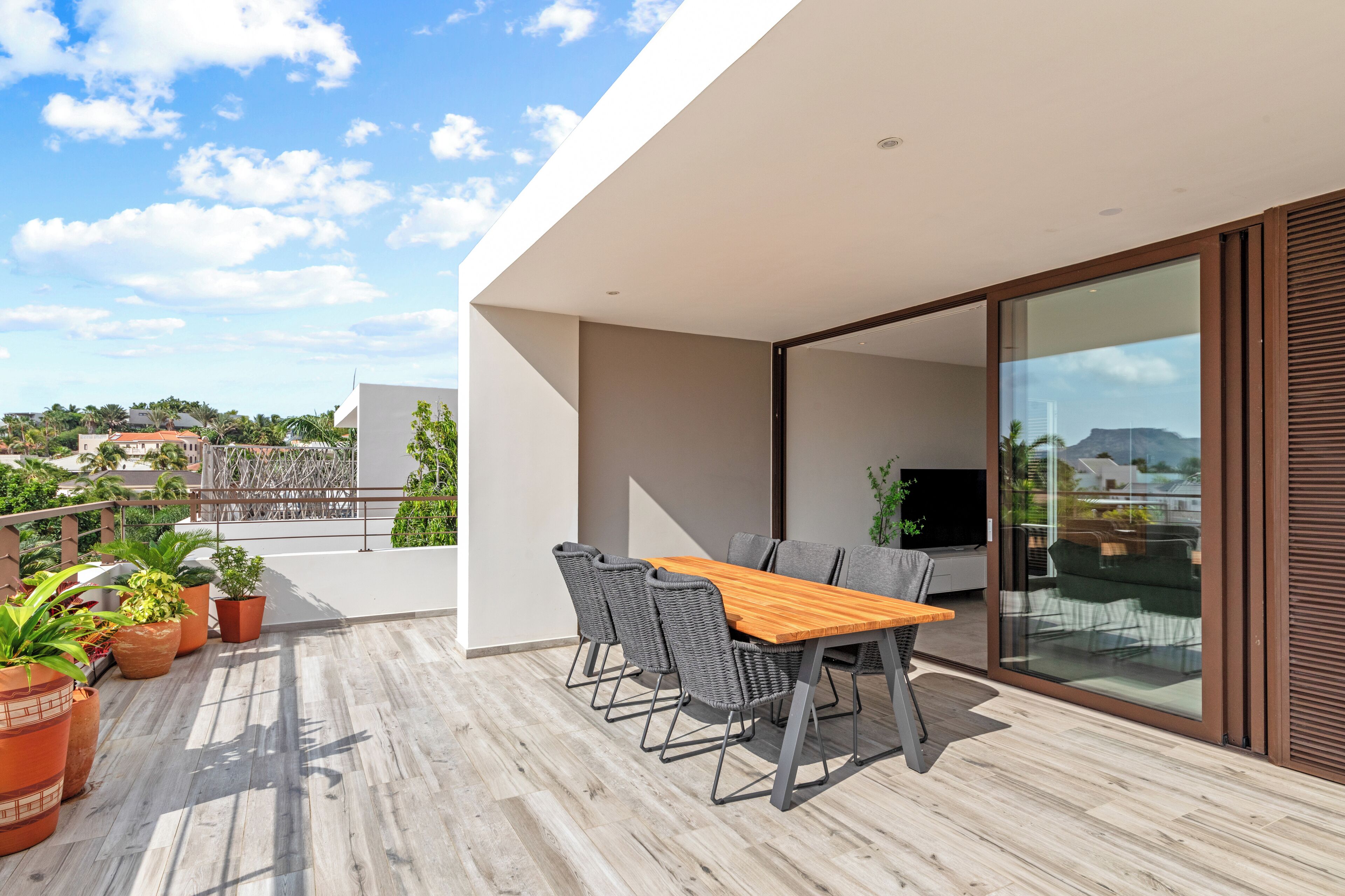 A modern outdoor dining area with a wooden table and chairs, surrounded by potted plants.