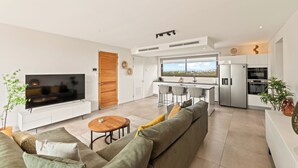 Uma sala de estar moderna com uma televisão grande, um sofá, um espaço de jantar e uma cozinha com vista.
