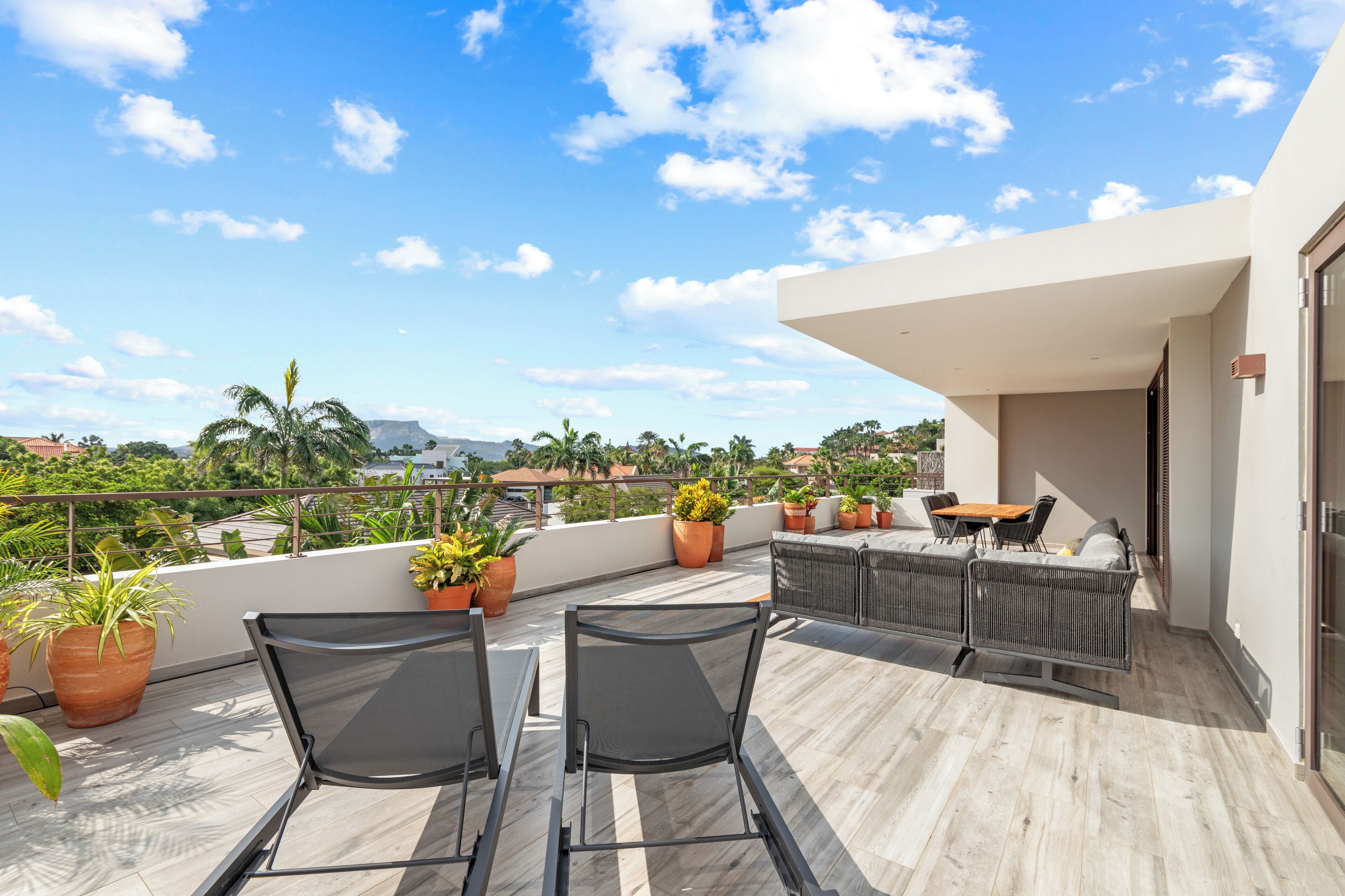 Terraço no telhado com duas cadeiras pretas, uma mesa e plantas em vasos.