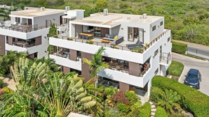 Um edifício residencial moderno, de vários andares, com varandas, áreas de estar ao ar livre e muita vegetação.