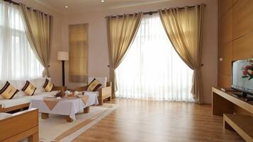 A hotel room with a sofa set, a table, a TV, and large windows with curtains.