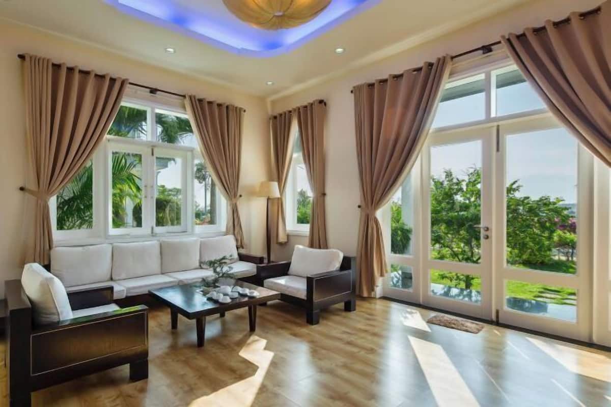 Un salón espacioso con un conjunto de sofás, una mesa de centro y ventanas grandes con cortinas.