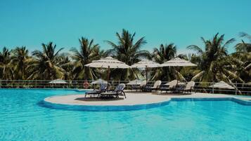 A swimming pool with lounge chairs and umbrellas, surrounded by palm trees.