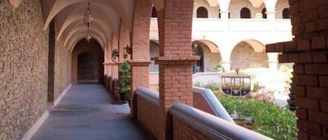Un pasillo con columnas y arcos de ladrillo que conduce a un patio con un tranvía antiguo.