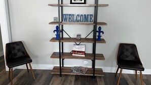 Una habitación con una estantería de madera que muestra un cartel de 'WELCOME', dos sillones tapizados de color negro y un cuadro en la pared.