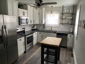 A modern kitchen with white cabinets, stainless steel appliances, a wooden table, and a ceiling fan. - Charming renovated 3-bedroom house walking distance to downtown Elizabethtown.  (Elizabethtown)