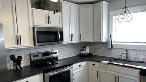Cocina moderna con armarios blancos, encimera negra, electrodomésticos de acero inoxidable y ventana con vistas.