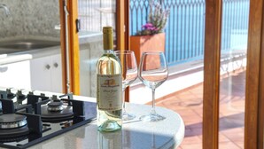 A bottle of wine and two glasses on a countertop with a view of a blue fence and plants outside.