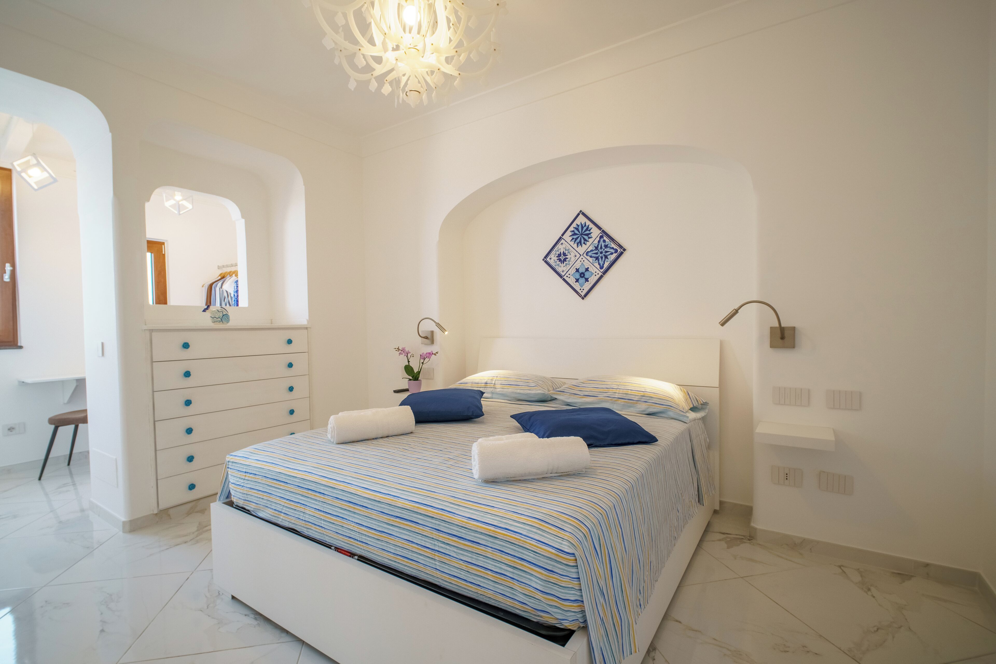 Une chambre à coucher comprenant un lit, une commode, un miroir et un carreau décoratif sur le mur.