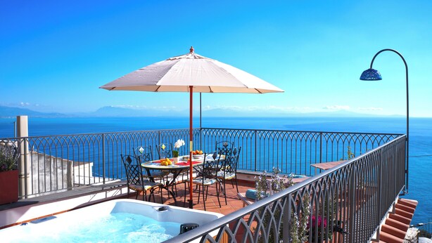 A balcony with a table, chairs, a hot tub, and a view of the sea.