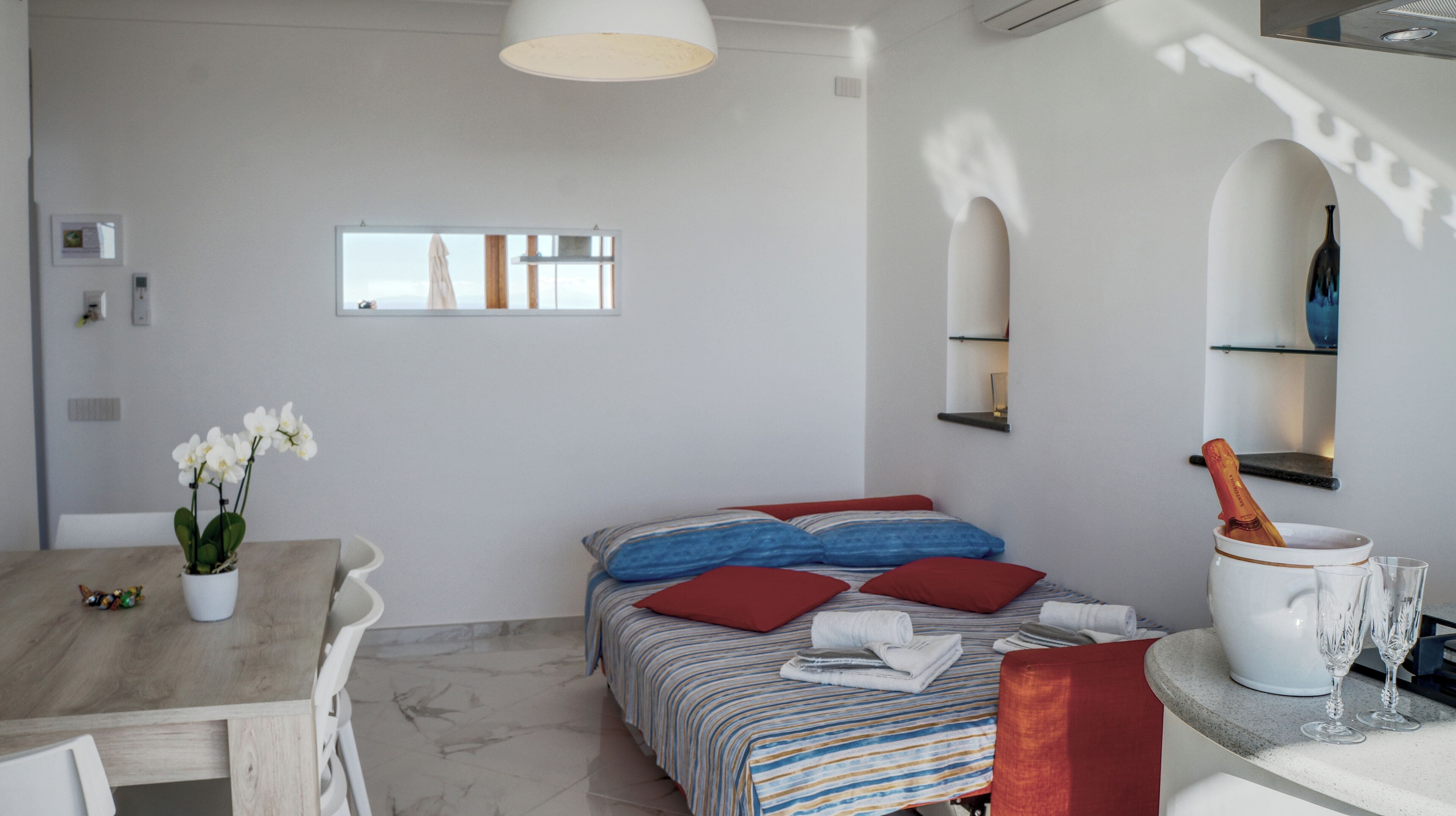 Une chambre à coucher avec un lit, des oreillers, une table de chevet, un vase et une bouteille.