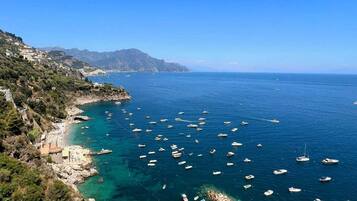 A coastal area with clear blue waters, boats, and a beach with umbrellas.