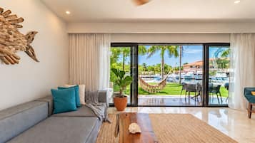 Una sala de estar moderna con un sofá, una mesa de centro de madera y vista a un puerto deportivo a través de puertas de cristal grandes.