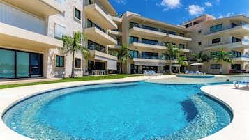 Un hotel moderno con una amplia piscina, varios balcones y palmeras.