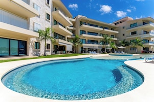 Un hotel moderno con una amplia piscina, varios balcones y palmeras.