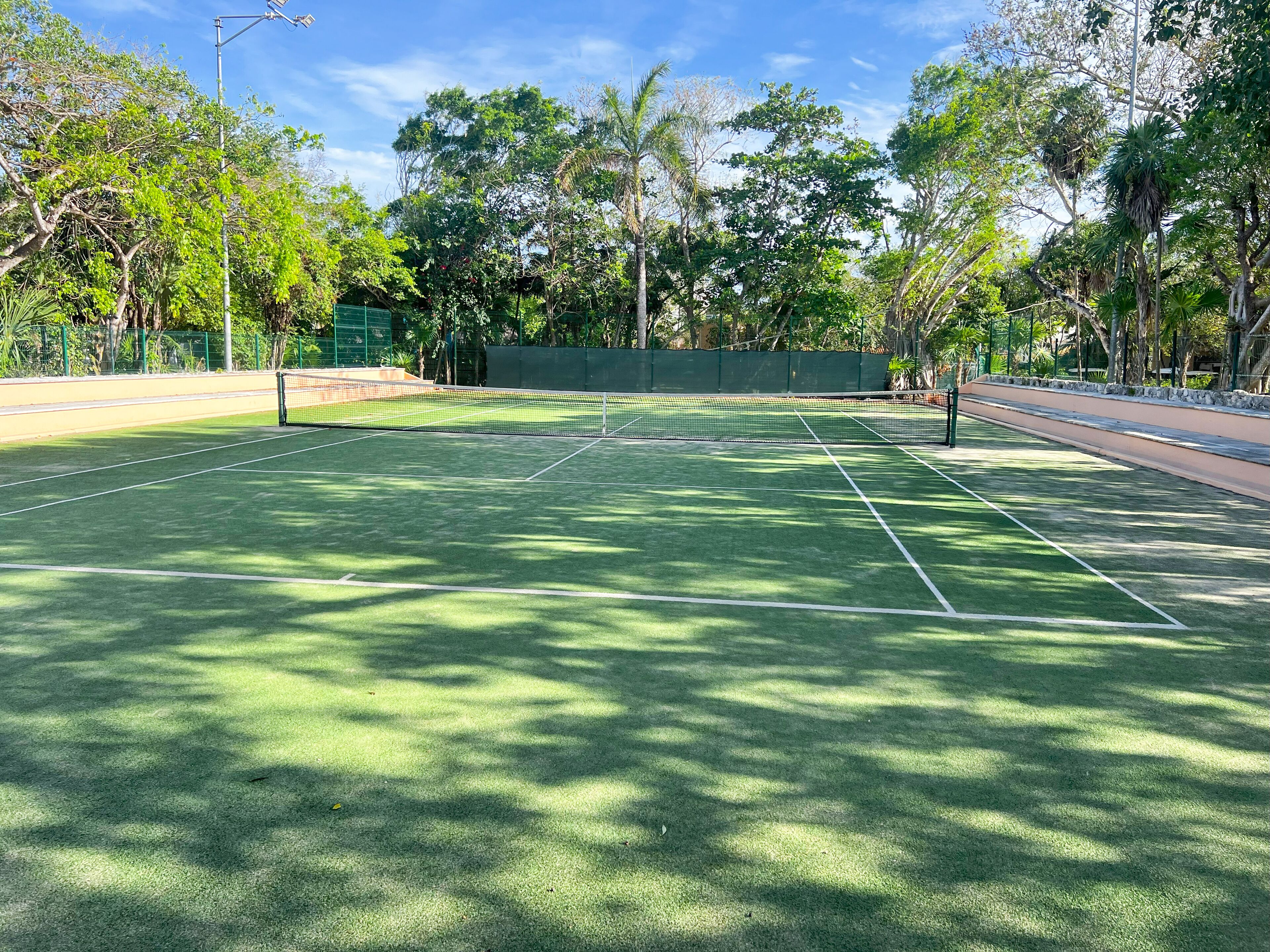 Una cancha de tenis con una red, rodeada de árboles y una valla verde.