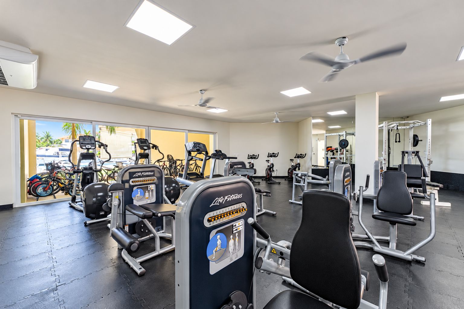Ein Fitnessstudio mit unterschiedlichen Trainingsgeräten, darunter Laufbänder, Kraftgeräte und Kurzhanteln.