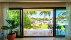 A room with a large sliding glass door leading to a pool area with a hammock, palm trees, and outdoor furniture. - Ground Floor Marina View Infinity Pool Private Terrace Puerto Aventuras (Puerto Aventuras)