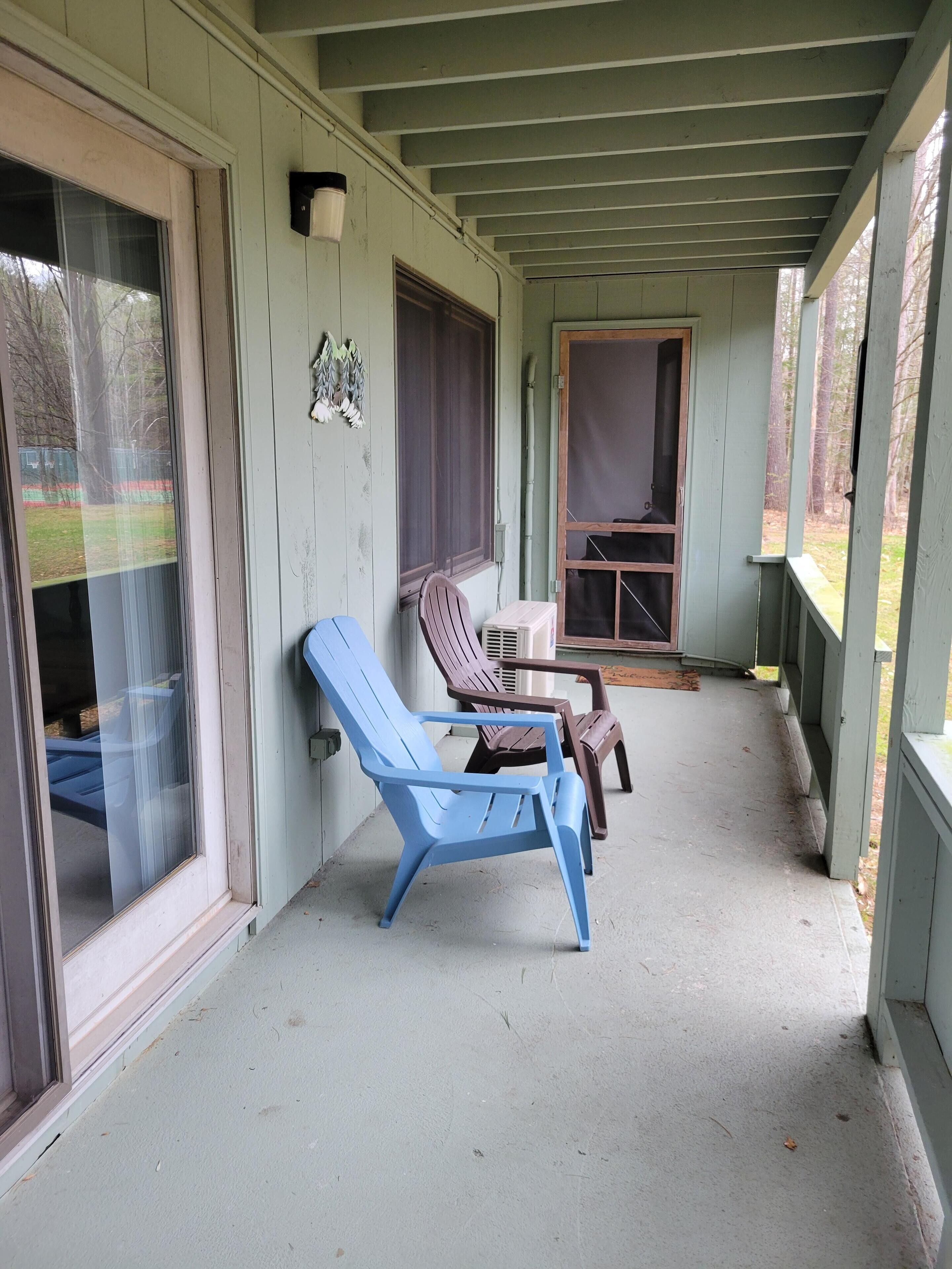 Een overdekt terras met twee stoelen, een tafeltje en een raam met uitzicht op bomen.