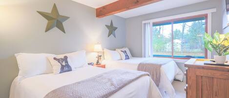 Une chambre avec deux lits, des décorations en forme d’étoiles sur le mur, une table de chevet avec une lampe, une commode en bois et une fenêtre donnant sur des arbres.