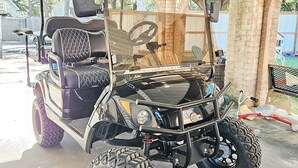 A black golf cart parked under a covered area with a brick wall and a wooden fence in the background. - Perfect Family Escape: Playground, Fire Pit, Games & Boat Parking Near Kemah! (Bacliff)