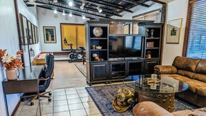 A modern living room with a large TV, leather sofa, and a coffee table. - Perfect Family Escape: Playground, Fire Pit, Games & Boat Parking Near Kemah! (Bacliff)
