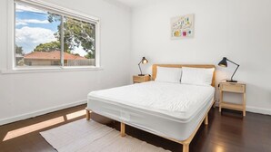 A bedroom with a large window, a bed with white bedding, two bedside tables with lamps, and a wall-mounted artwork. - Bonbeach Beauty: Relaxation Haven in Bonbeach! (Bonbeach)