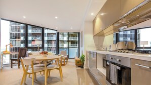 Una cocina moderna con horno empotrado, un comedor con mesa y sillas, y ventanas amplias que ofrecen vistas a la ciudad.