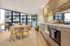 Eine moderne Küche mit Einbauofen, ein Essbereich mit Tisch und Stühlen sowie große Fenster mit Blick auf die umliegenden Gebäude.