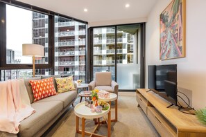 Un salon moderne comprenant un canapé, un fauteuil, une table basse, un téléviseur et un balcon offrant une vue sur un immeuble de grande hauteur.