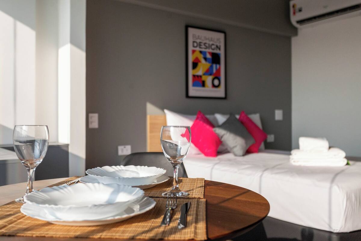 A neatly arranged dining table with plates and glasses, a bed with pillows, and a wall with a poster.