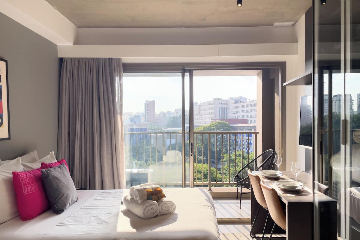 A hotel room with a large bed, a dining area, and a balcony with a city view.