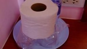 A roll of toilet paper on a plastic plate, two water bottles, and a power outlet on a wooden surface. - Pama Resort (Rayong City)