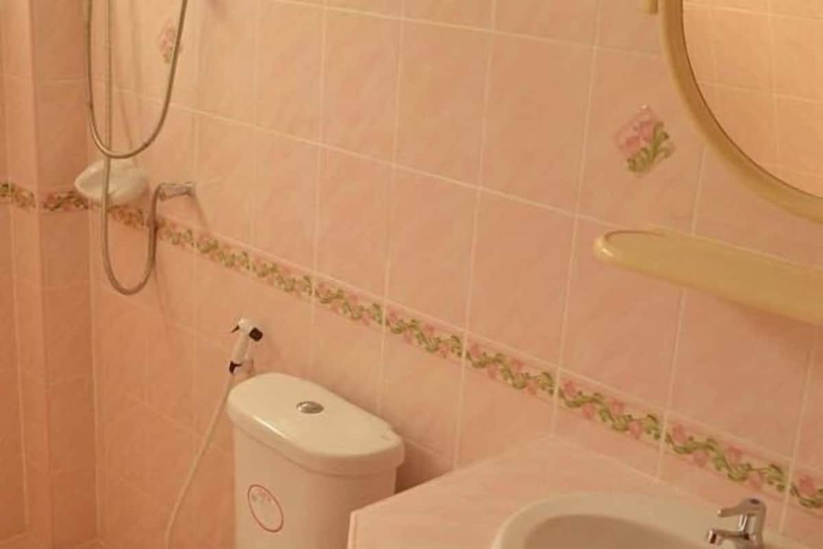 Ein Badezimmer mit rosa gefliesten Wänden, einer Toilette, einem Waschbecken und einer Dusche.