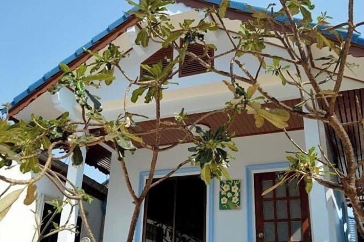A building with a white facade, a brown roof, and a window with a green decorative panel.