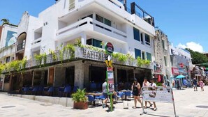 A white building with a restaurant named "EATITAM" on the ground floor, featuring outdoor seating and potted plants. - Room with King bed in BLVD HOTEL, fifth avenue (Playa del Carmen)