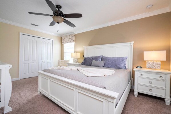 Une chambre à coucher avec un lit, des tables de chevet, un ventilateur de plafond et une porte.