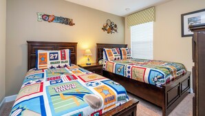 Un dormitorio con dos camas, una mesita de noche, una lámpara y decoración de pared con temática deportiva.
