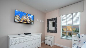 Un dormitorio con televisión mostrando un castillo, un aparador, un espejo y una ventana con persianas.