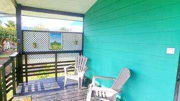 A covered porch with two Adirondack chairs, a wooden deck, and a green wall.