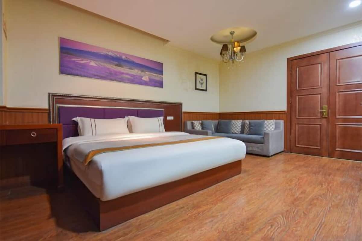 A bedroom with a large bed, a sofa, a wooden wardrobe, and a painting on the wall.