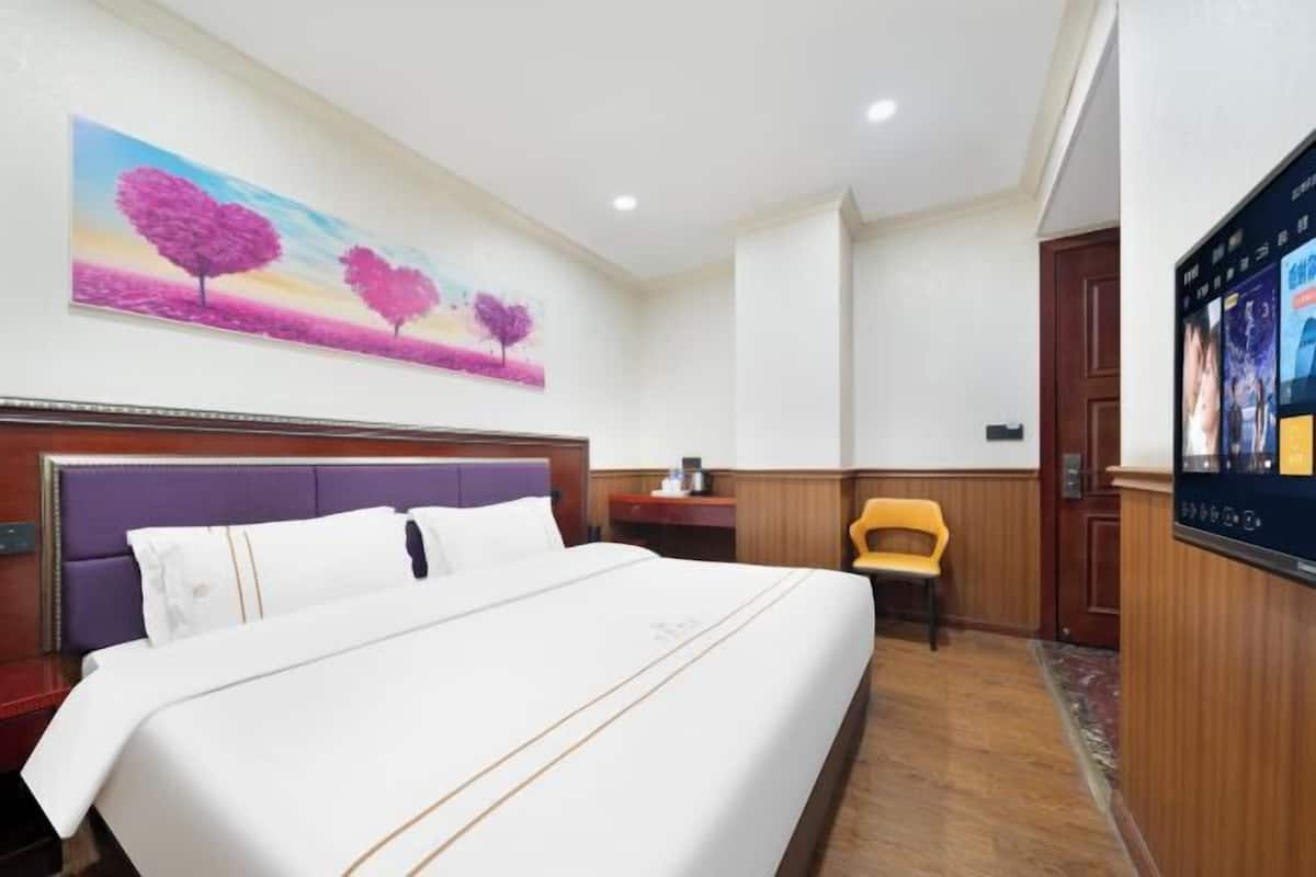 A hotel room with a bed, a desk, a chair, a TV, and a painting on the wall.