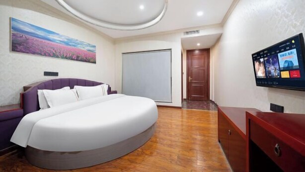 Una habitación de hotel moderna con una cama curvada, un cuadro grande en la pared, un televisor y piso de madera.