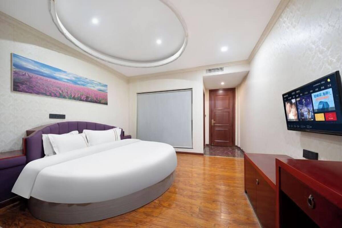 A modern hotel room with a curved bed, a large painting on the wall, a television, and a wooden floor.