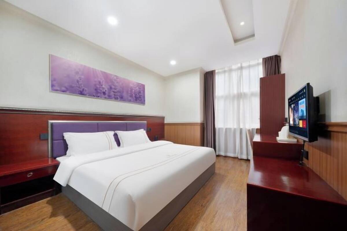 A hotel room with a large bed, a television, a desk, and a purple artwork on the wall.